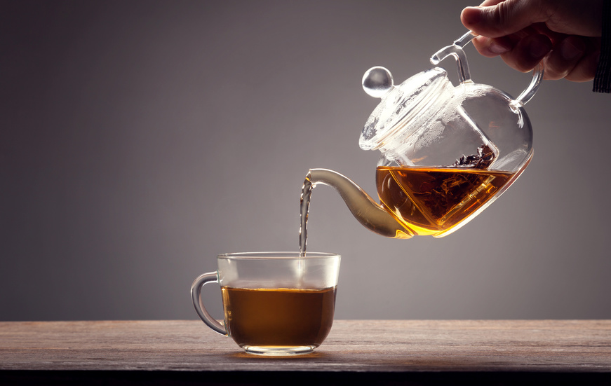 glass tea pot pouring into a glass cup on a wood table