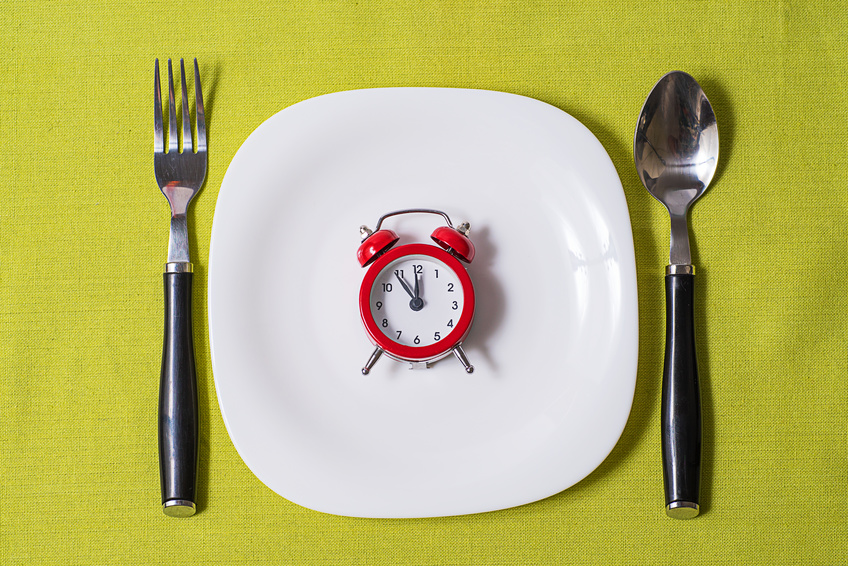 small clock on a white plate on grey tablecloth with fork and spoon on either side of plate